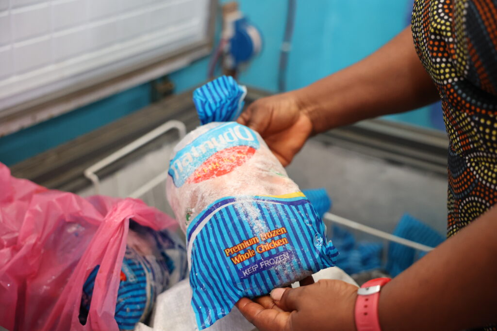 A woman holds a frozen chicken over an open freezer.