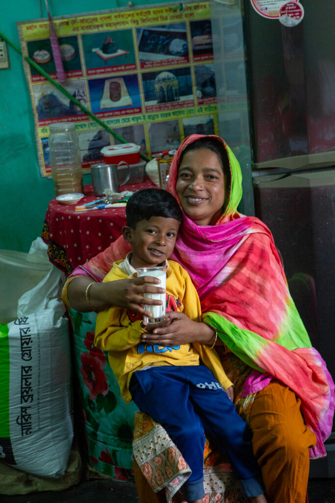 A woman helps her young son drink a glass of milk.