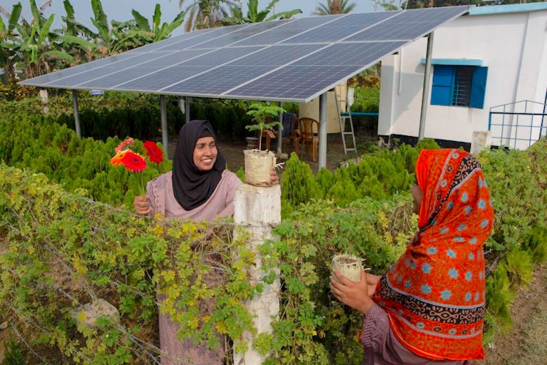 Asma Khatun, 36, (left) talks to Zahirul Islam outside the Gerbera nari unnayan Women Cooperative Limited solar panel site in Panisara village, Bangladesh on December 30, 2024. The solar panels help run power to the water irrigation system.