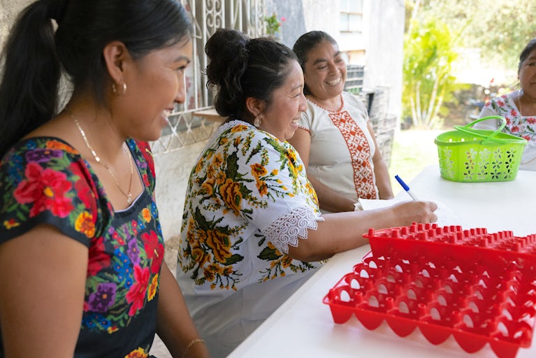 Women sitting at a table with empty egg cartons, smiling to each other.