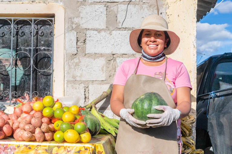 A woman smiles while holding a watermelon.
