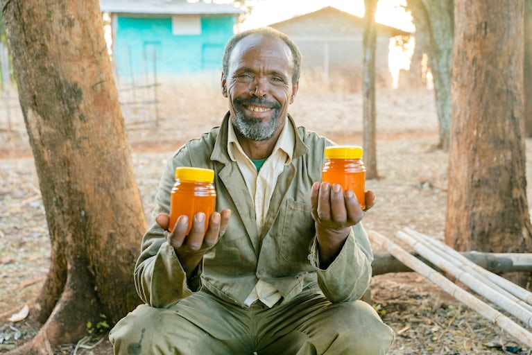 An Ethiopian man smiling and holding a jar of honey in each hand.