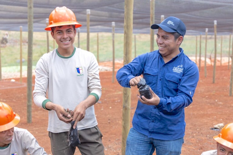 Henry Choc Xol smiles and Heifer staff member Braulio Paau shows him how to prepare bags of soil for seedlings.