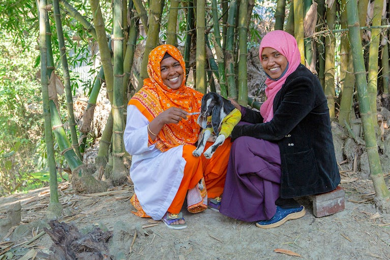 Two smiling women with a goat