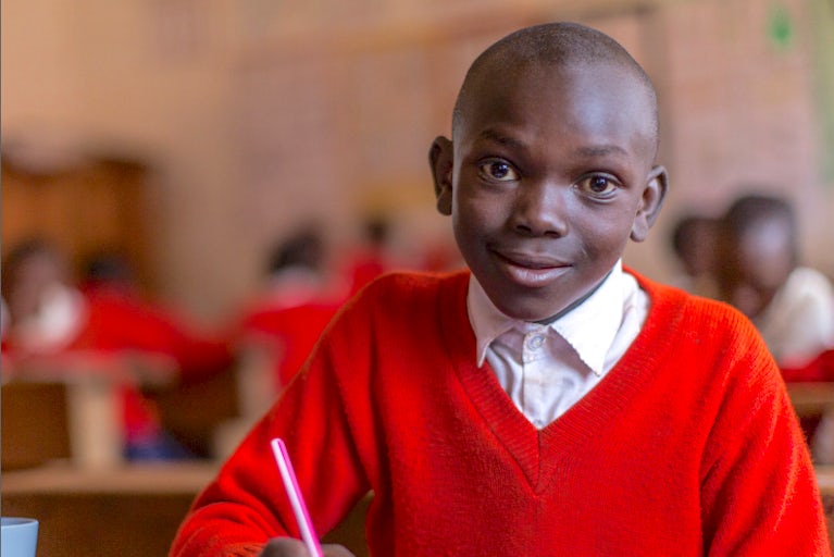 Young boy wearing a red sweater and working on a school assignment in a classroom.