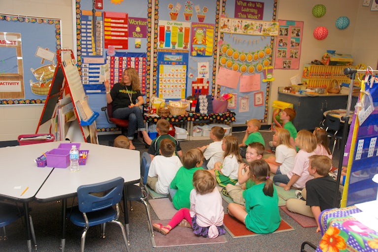 Teacher seated with classroom of young children sitting on floor during story time.