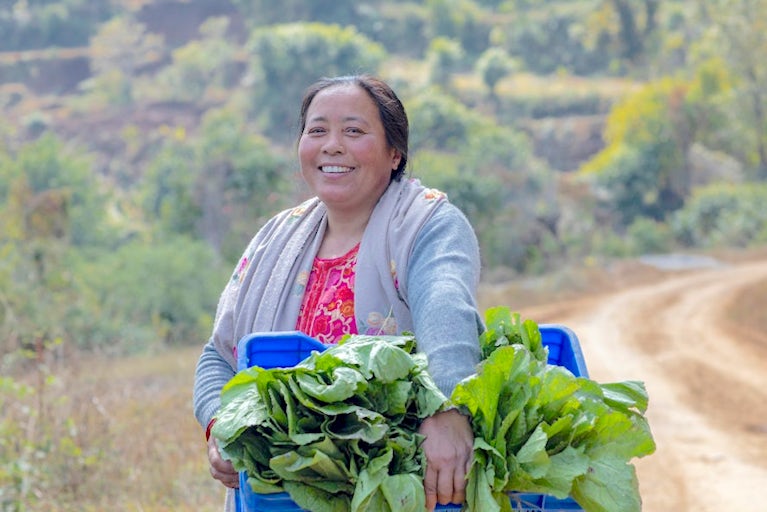 Smiling woman holds crate of fresh leafy greens.