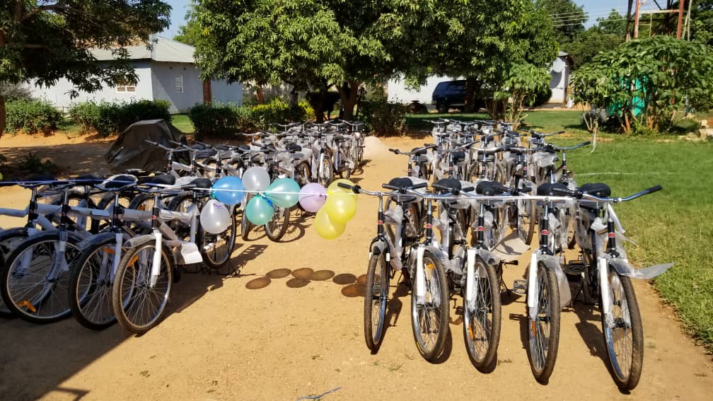 Many bikes, set to be distributed to local farmers, stand on a dirt road.