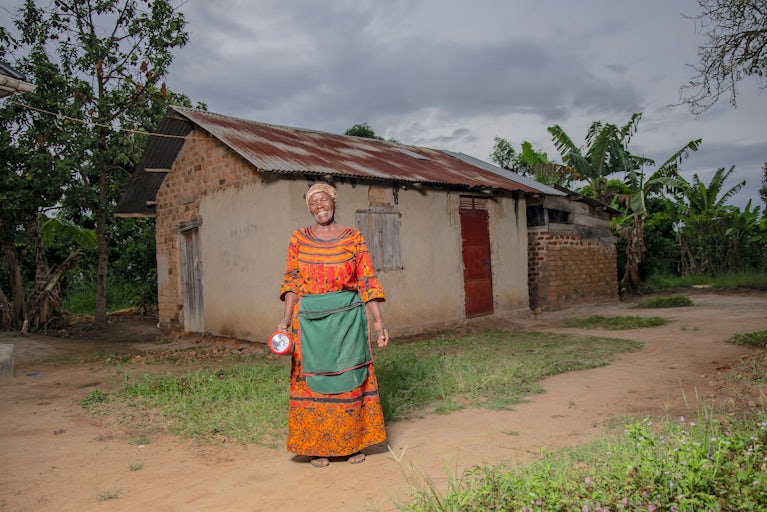 A woman stands outside her home holding a solar-powered flashlight.