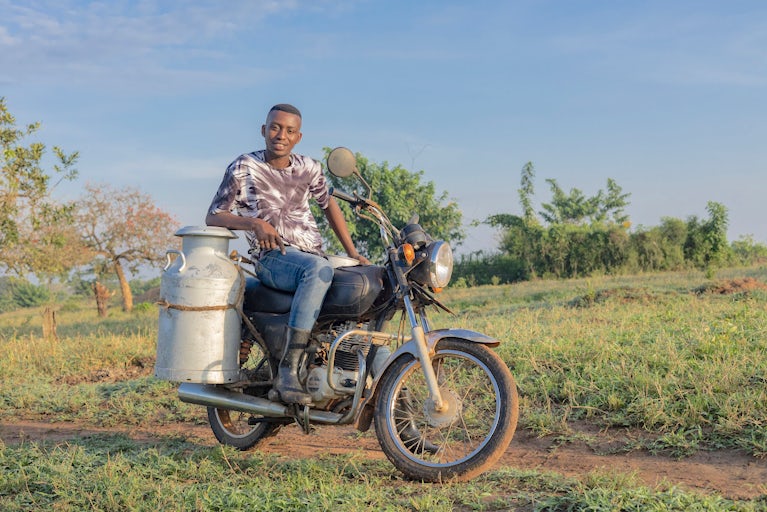 A man sits on a motorcycle with a large milk can strapped to the side.