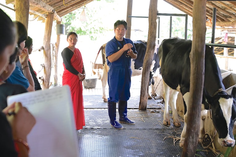 Veteranarian addressing group of people while standing next to a cow.