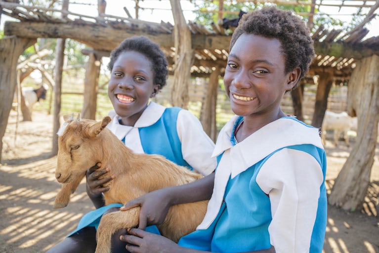 Prudence Kaumbo, 13, (left) and her cousin Emmy Nswana, 13, with one of the family's goats.
